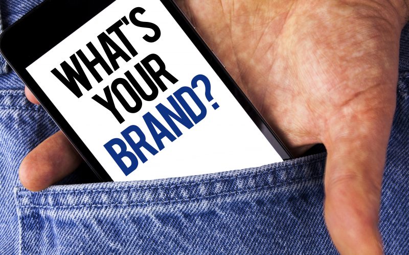 Writing note showing  What Is Your Brand Question. Business photo showcasing Define Individual trademark Identify Company written Mobile phone screen holding by man the Jeans background.